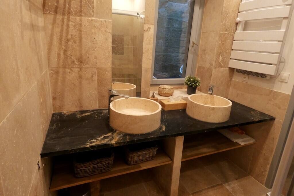 Een badkamer met twee ronde wastafels, een spiegel en een raam met uitzicht op een stenen muur.