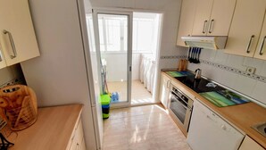 Une cuisine équipée d’un réfrigérateur, d’une cuisinière, d’un four et d’un évier. Il y a une fenêtre et une porte donnant sur un balcon.