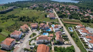 Vue aérienne d’un quartier résidentiel situé sur la côte, avec des maisons, une piscine et une grande étendue d’eau en arrière-plan.