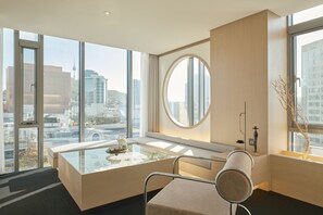 A modern hotel room with a large window, a round mirror, a glass table, and a minimalist design. - UH Suite The Seoul (Seoul)