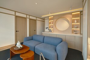 Una habitación de hotel moderna con un sofá azul, una mesa de centro de madera y un estante empotrado con adornos.