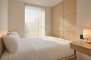 A hotel room with a bed, a bedside table with a lamp, and a window with blinds. - UH Suite The Seoul (Seoul)