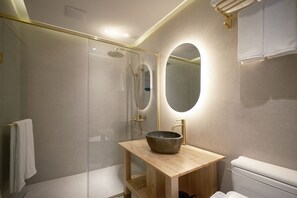 Un baño moderno con ducha de vidrio, tocador de madera con lavabo y un espejo grande.