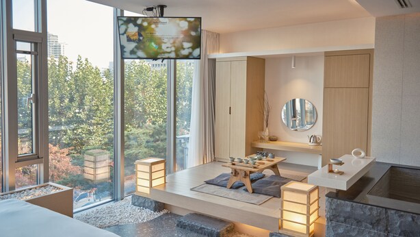 A modern hotel room with a large window, a wooden table with bowls, a mirror, and a stone accent wall. - UH Suite The Seoul (Seoul)