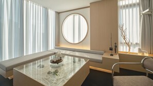 A modern hotel room with a glass coffee table, a round mirror, a sofa, and a chair. - UH Suite The Seoul (Seoul)