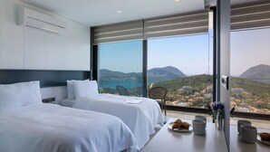 Habitación de hotel con dos camas, una mesa de comedor y un plato de cruasanes, con vistas a un paisaje montañoso.