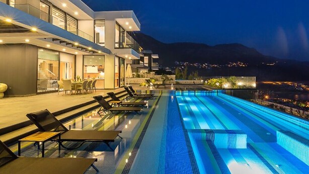 Un hotel moderno con piscina infinita en la azotea, mobiliario exterior y vistas a la ciudad de noche.