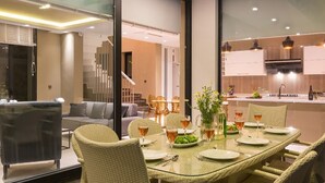 Un moderno comedor con una mesa de vidrio preparada para cuatro personas, rodeado de sillas de mimbre.