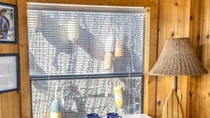 Un interior de madera con una mesa y sillas blancas, una lámpara y una ventana con persianas.