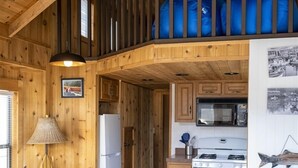 Un interior acogedor de cabaña con comedor, cocina y un dormitorio en la buhardilla.