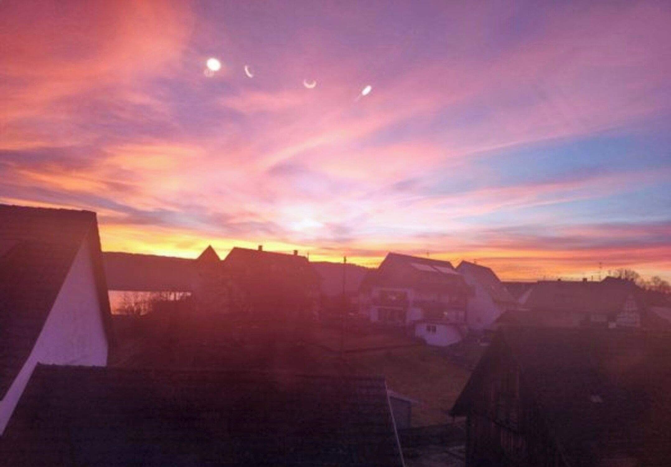A sunset over a residential area with houses and a clear sky.
