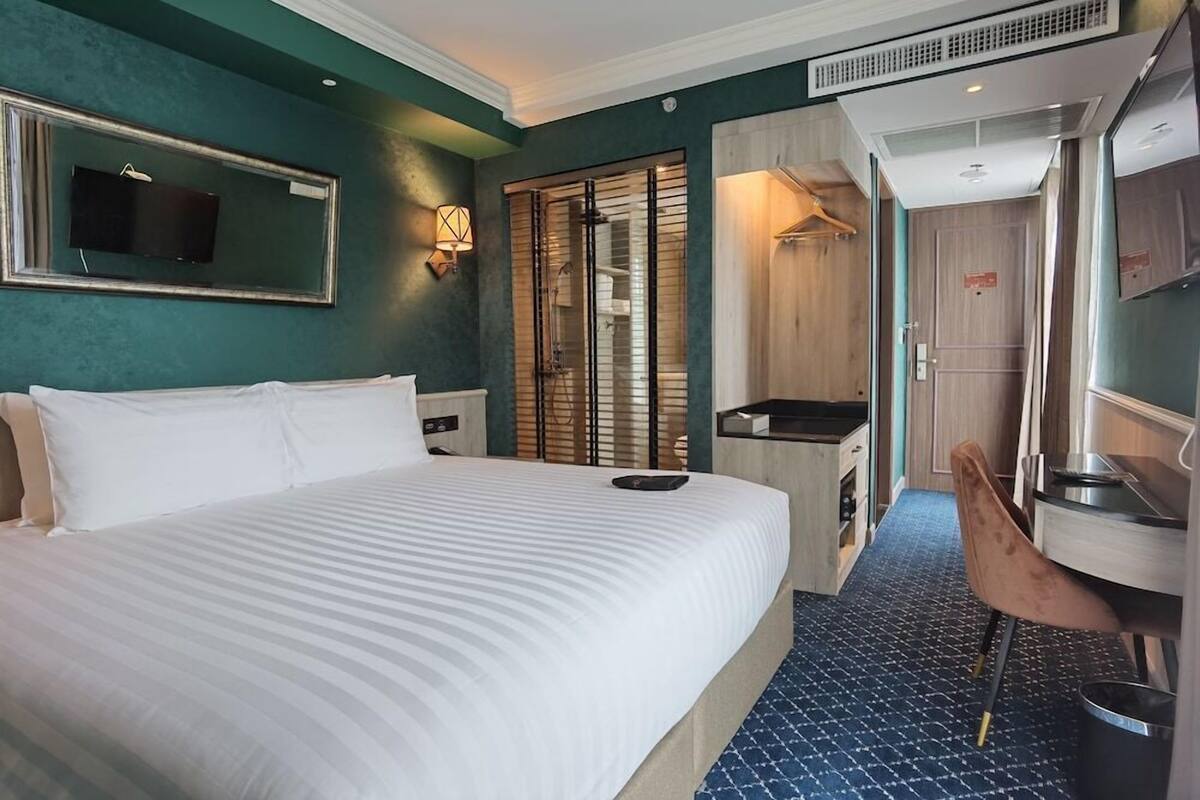 A hotel room with a large bed, a small kitchenette, a mirror, and a shower area.