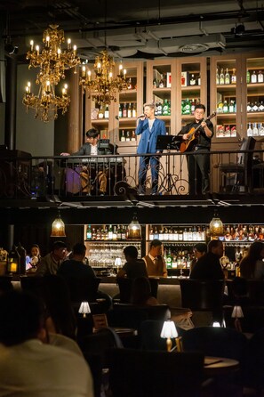 Un bar con una banda tocando en vivo en un balcón, rodeado de clientes sentados en mesas.