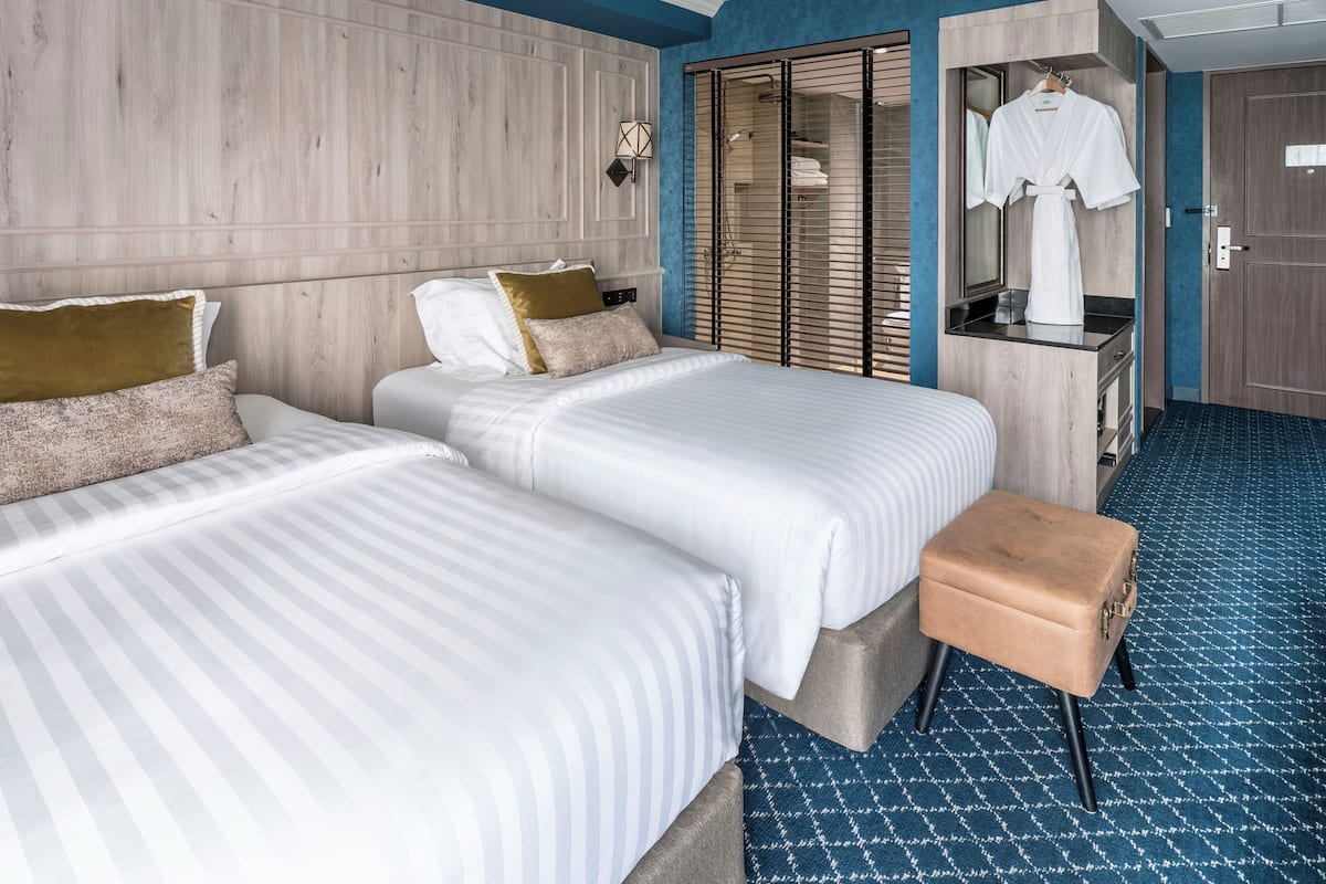 A hotel room with two beds, a small bench, a walk-in closet, and a bathroom with a shower.