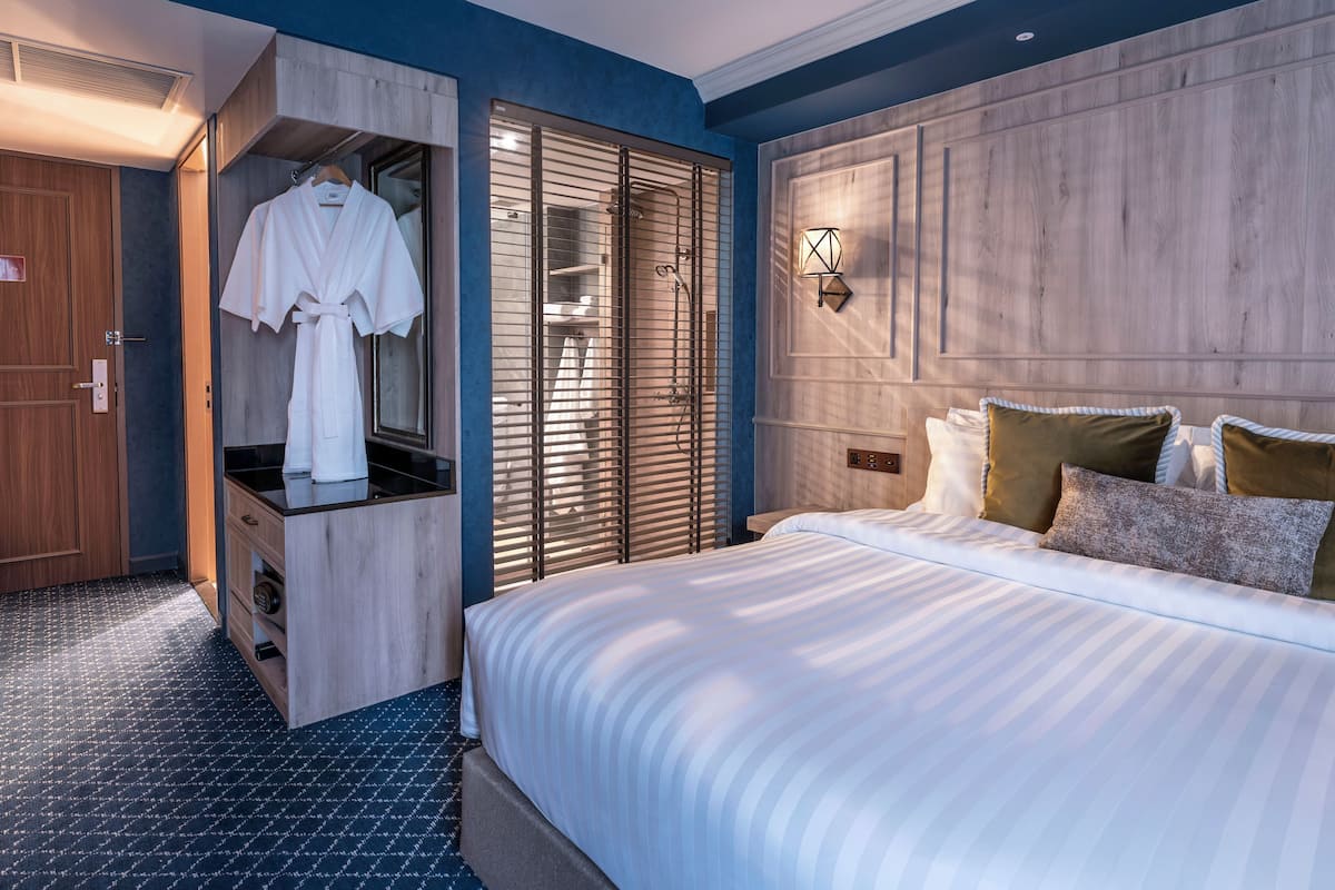 A hotel room with a large bed, a wooden wardrobe, a robe hanging on the door, and a shower area.