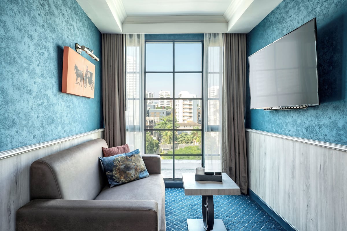 A modern hotel room with a large window, a sofa, a small table, and a mounted TV.