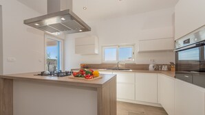 A modern kitchen with white cabinets, a wooden island, and a built-in oven. - Villa Defiance (Benkovac)