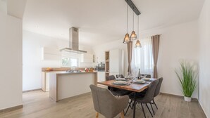 A modern kitchen with a central island, a dining area with a wooden table and chairs, and a large potted plant. - Villa Defiance (Benkovac)