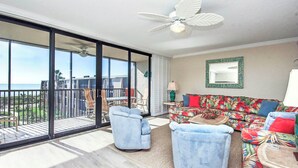 A spacious balcony with a view of the ocean, a ceiling fan, and a tropical-themed sofa set.