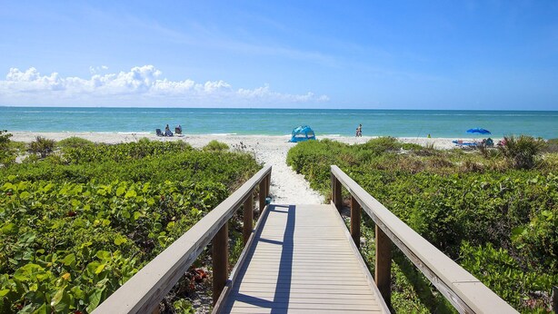 A wooden boardwalk leading to a beach with clear skies and calm waters.