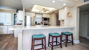 A modern kitchen with a central island, bar stools, a ceiling fan, and a view into the adjacent dining area.