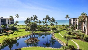 A resort with a central pond, palm trees, and a view of the ocean.