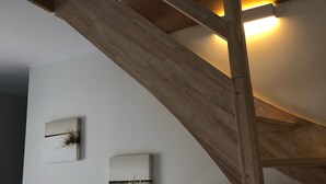 Un escalier en bois avec un puits de lumière, un mur blanc orné de deux œuvres d’art et un fauteuil suspendu blanc.
