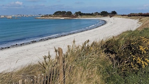 Une plage de sable avec une clôture en bois au premier plan, un ciel bleu dégagé et une mer calme.