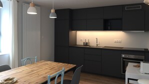 Une cuisine moderne avec des meubles de couleur sombre, une table à manger en bois et des luminaires suspendus.