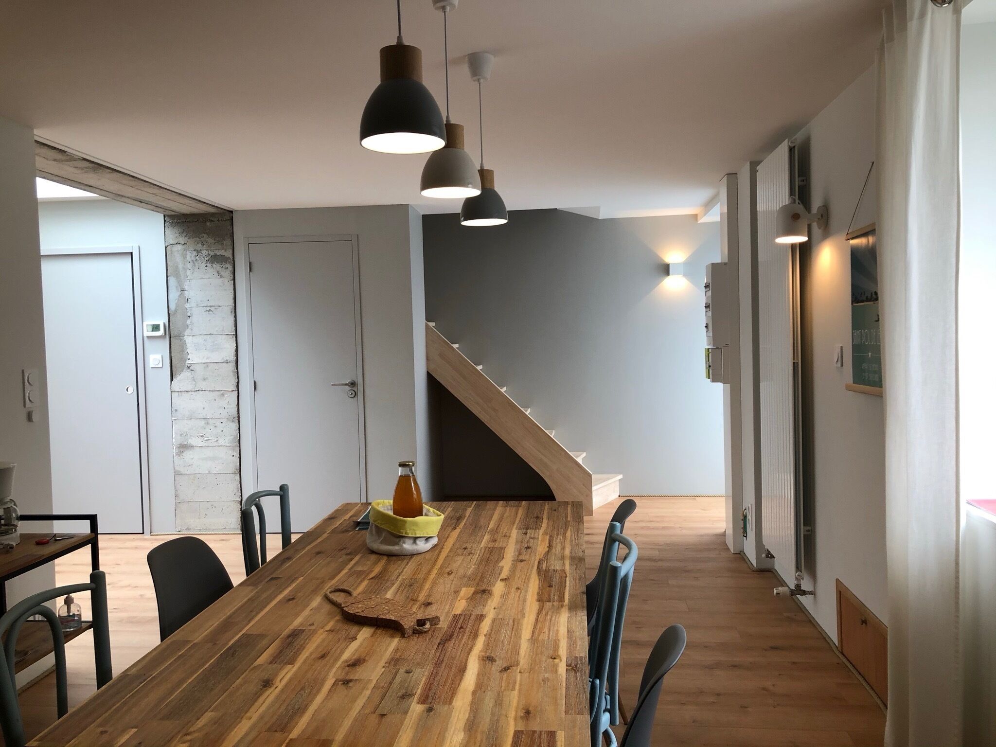 Une cuisine moderne avec une table en bois, des luminaires suspendus et un escalier menant à un autre niveau.