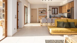 A modern kitchen with wooden cabinets, a dining area with a table and chairs, and a yellow sofa in the living room.