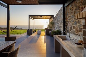 An outdoor patio with a stone wall, a pergola, and a view of the ocean. - Dream vacation with stunning sunsets at Villa Violetta (Kissamos)