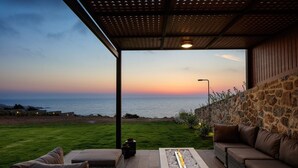 A patio with a stone wall, a fire pit, and outdoor furniture overlooking the sea at sunset.