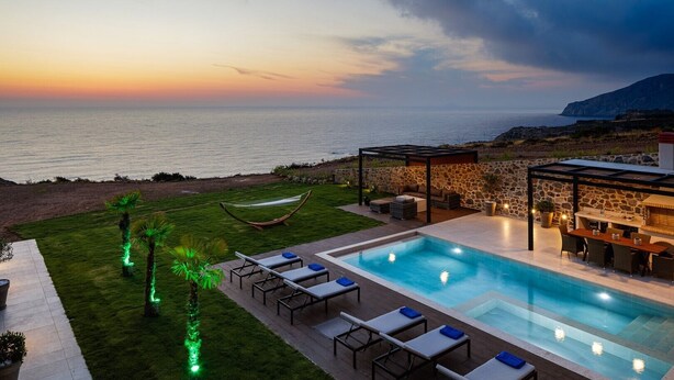 A pool area with lounge chairs and a hammock, overlooking a beach with a sunset view.