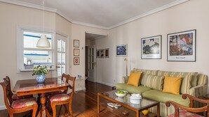 Una sala de estar con una mesa de comedor de madera, sillas, una mesa de centro de vidrio, un sofá verde y vistas a la cocina a través de una puerta abierta.