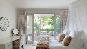 Quarto com cama, escrivaninha, cadeira, mesa de cabeceira, relógio e janela com cortinas.