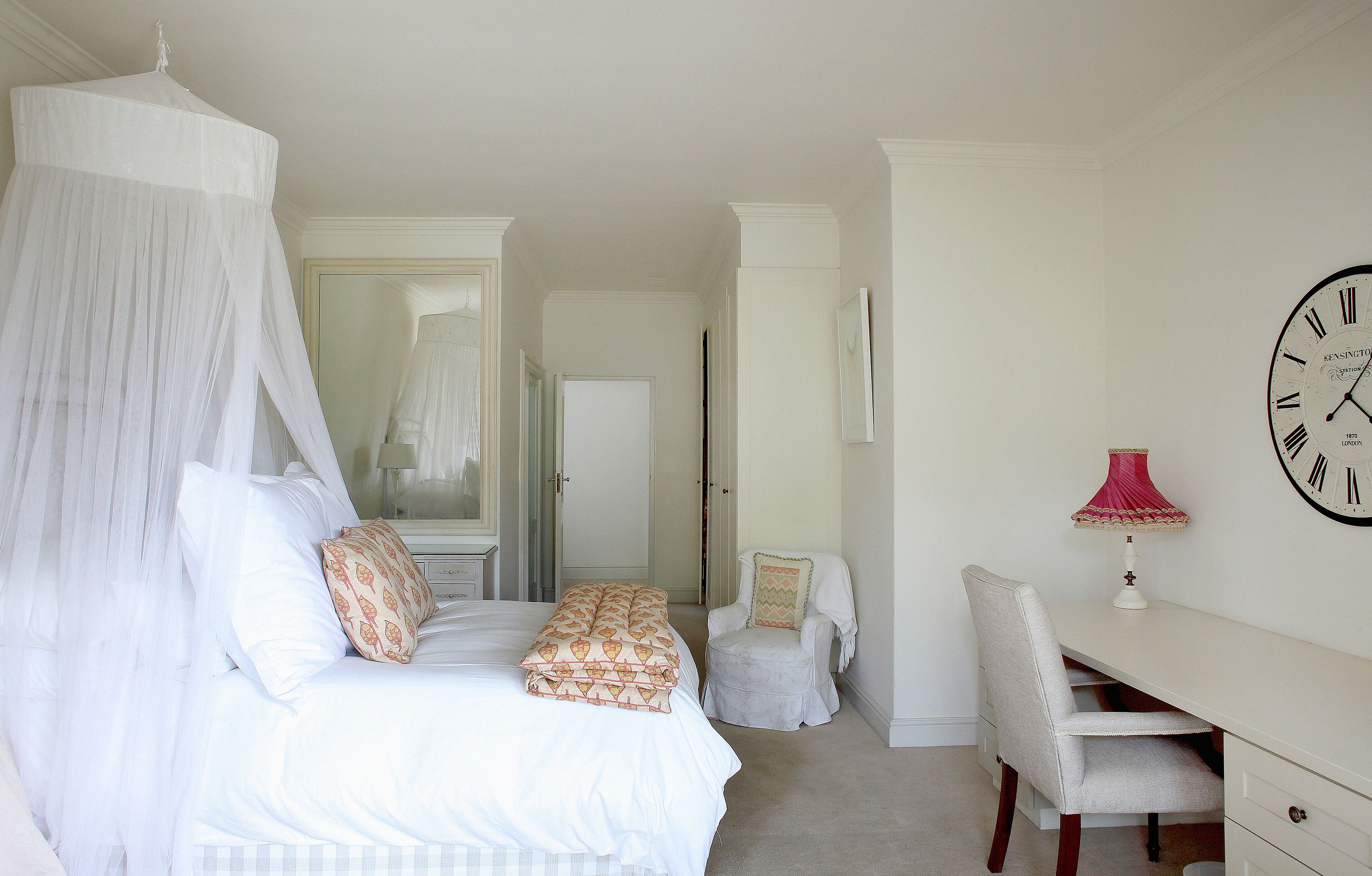 A bedroom with a canopy bed, a desk, a chair, and a clock on the wall.