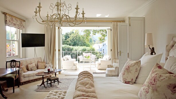 Um quarto espaçoso com uma cama grande, um espaço de estar com sofá e cadeiras, uma mesa de jantar e uma varanda com móveis de exterior.