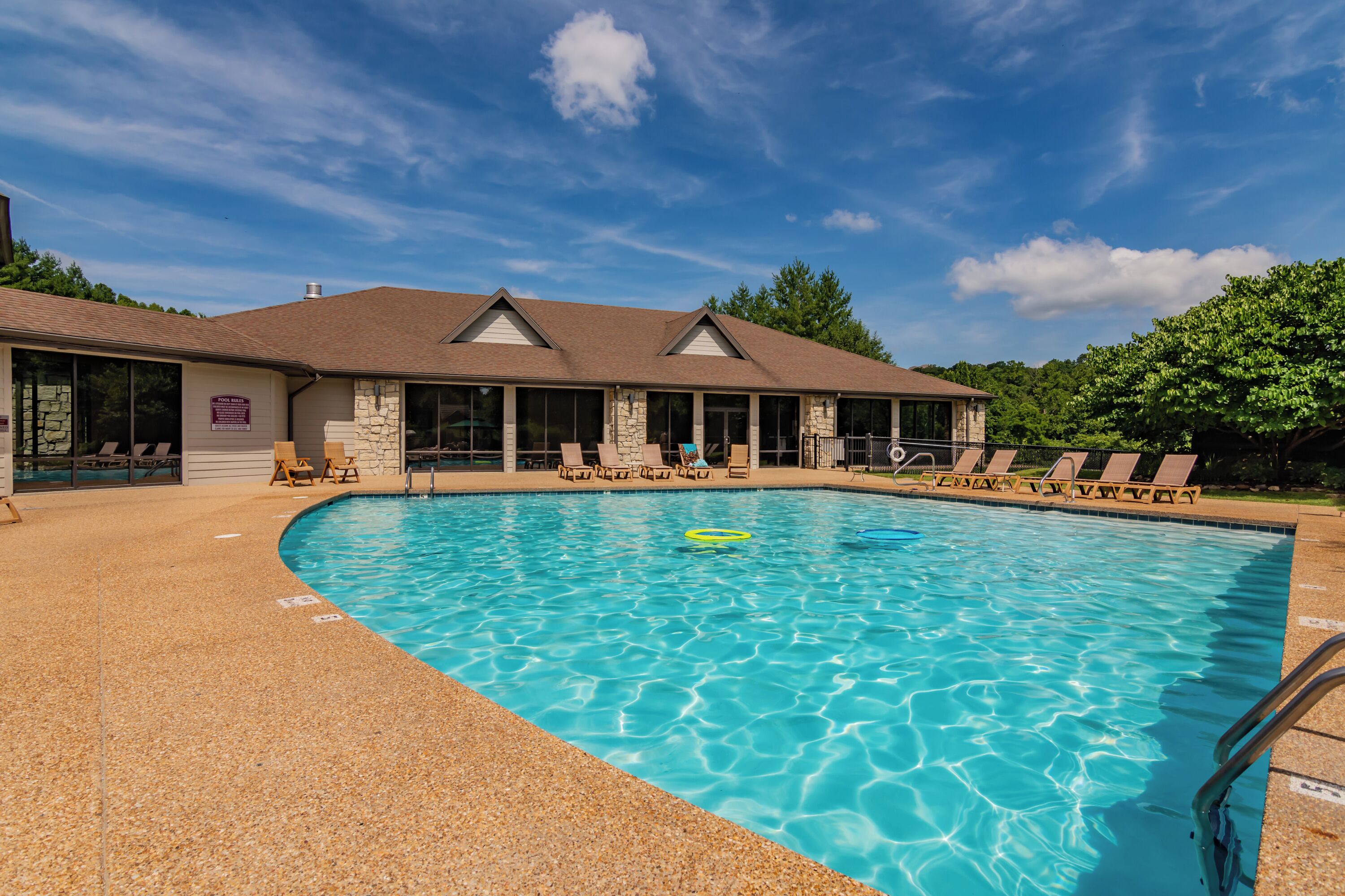 A swimming pool with lounge chairs and a building with a stone facade and a sloped roof.