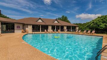 A swimming pool with lounge chairs and a building with a stone facade and a sloped roof.
