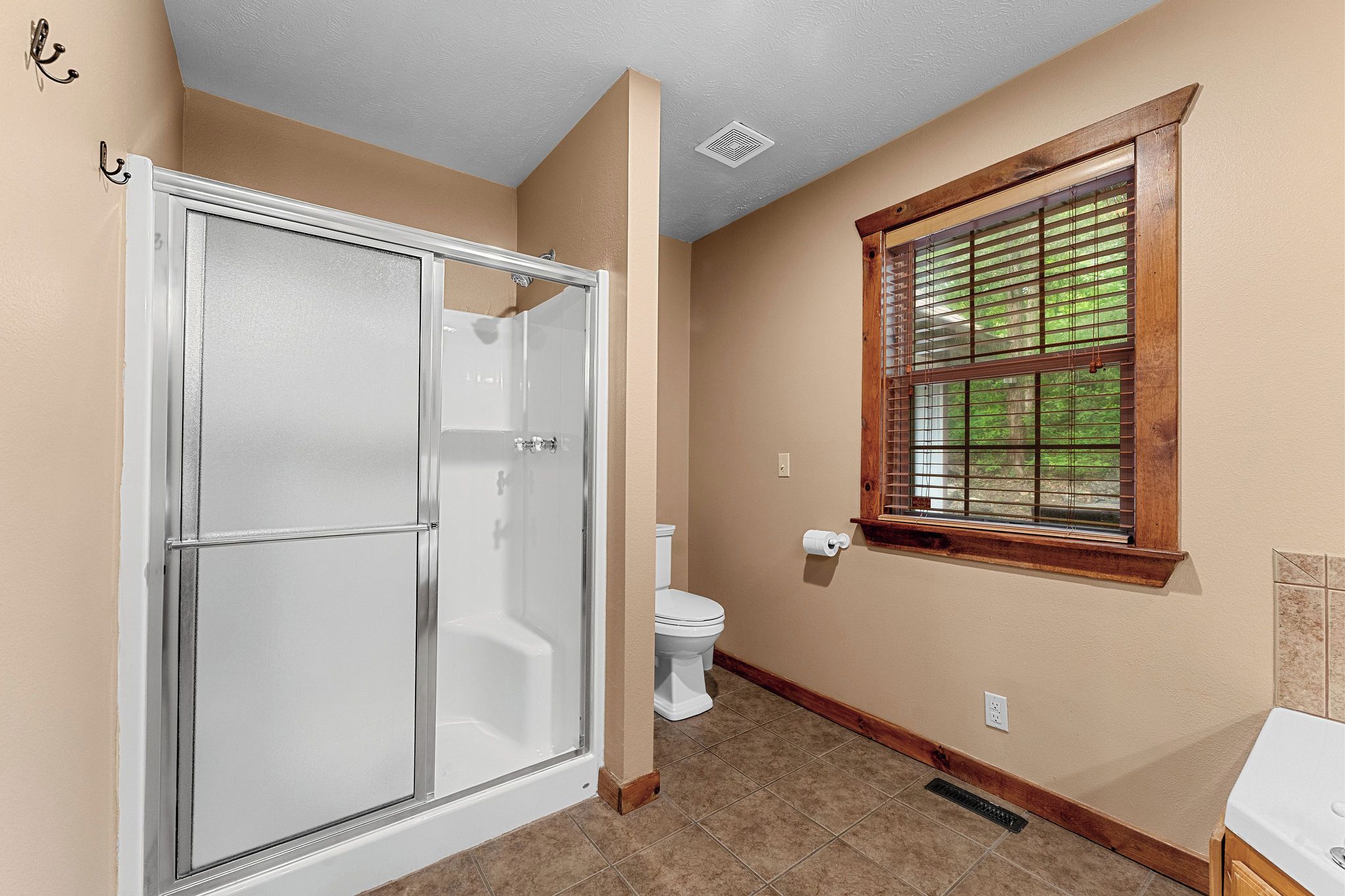 A bathroom with a glass shower enclosure, a toilet, and a window with blinds.