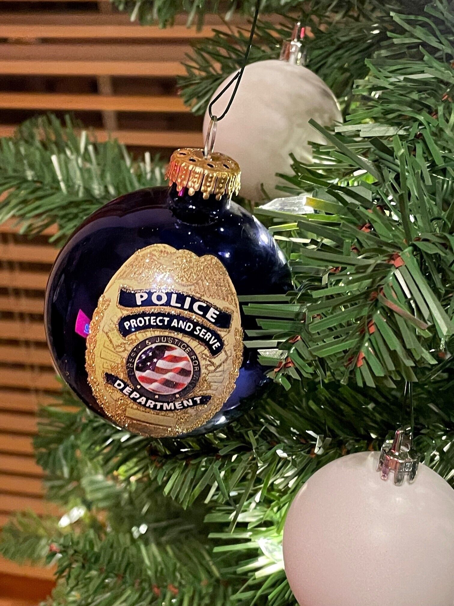 A Christmas ornament shaped like a police badge with text "POLICE PROTECT AND SERVE JUSTICE FOR DEPARTMENT" on a Christmas tree.