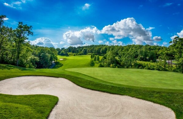 Un parcours de golf doté d’un bunker de sable, d’une pelouse bien entretenue et d’un ciel bleu dégagé.