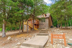 A lodge with a stone exterior, wooden deck, and a staircase leading to the entrance.