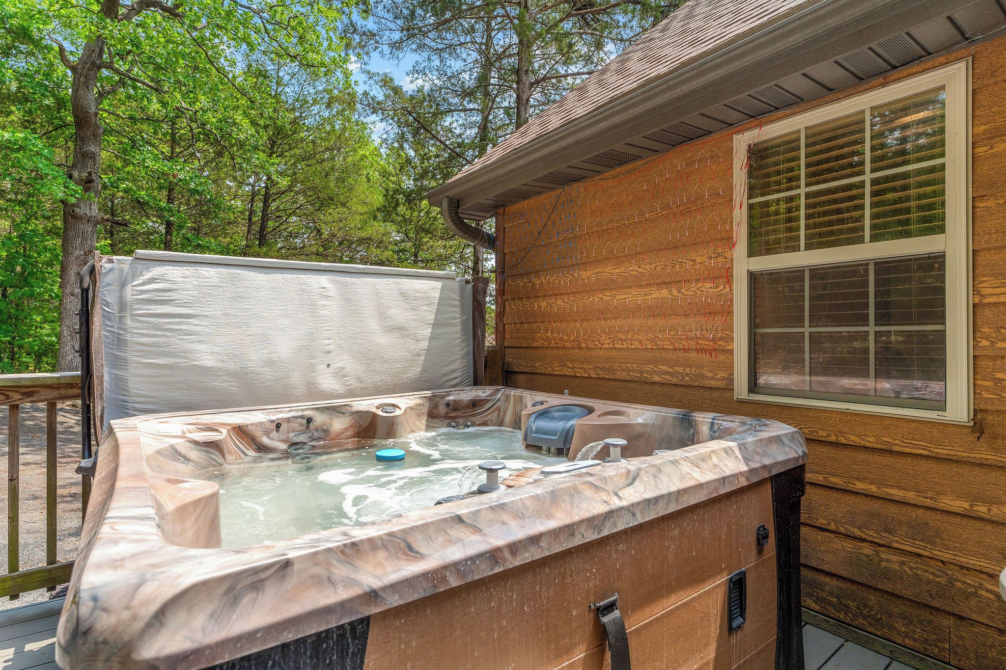 Un bain à remous avec un revêtement extérieur en bois, une fenêtre avec des stores et une terrasse en bois.