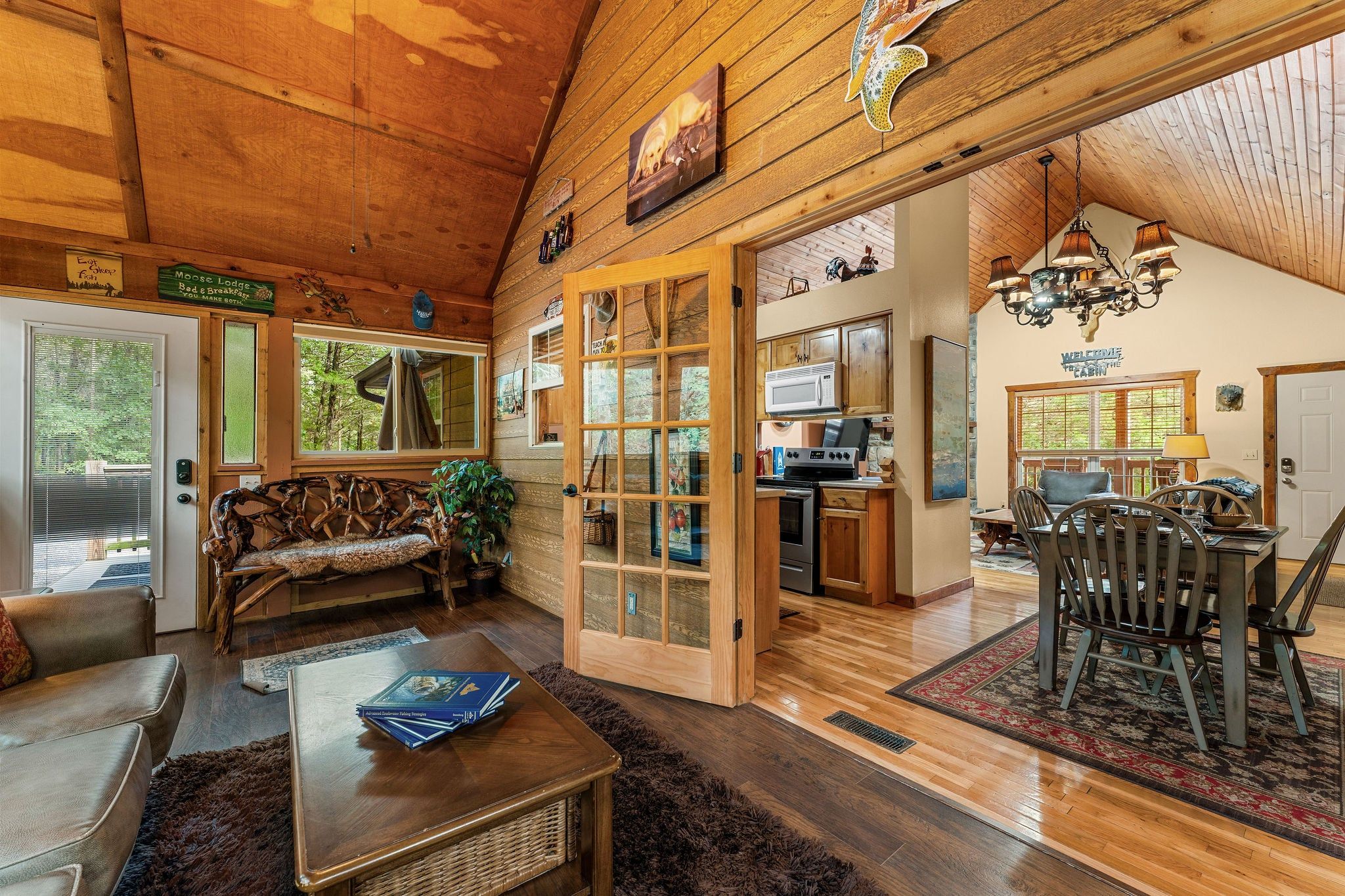 A cozy lodge interior with a dining area, kitchen, and a large wooden door leading to a deck.