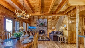 L’intérieur d’un chalet en bois comprend un coin repas, une cheminée, un canapé et un escalier.
