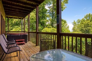 A covered outdoor deck with wooden flooring, a glass table, and metal chairs.