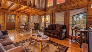 Un intérieur de cabine spacieux, avec un revêtement en bois, un coin repas, un salon doté d’un canapé et d’un téléviseur, et de grandes fenêtres.