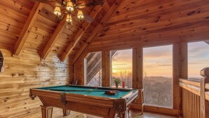 Un intérieur en bois avec une table de billard, de grandes fenêtres et une vue sur le paysage.